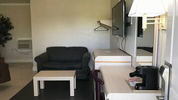 Ein kleines Hotelzimmer mit einer Sitzecke, einem Tisch, einem Schreibtisch mit Lampe, einem Fernseher und einem Spiegel.