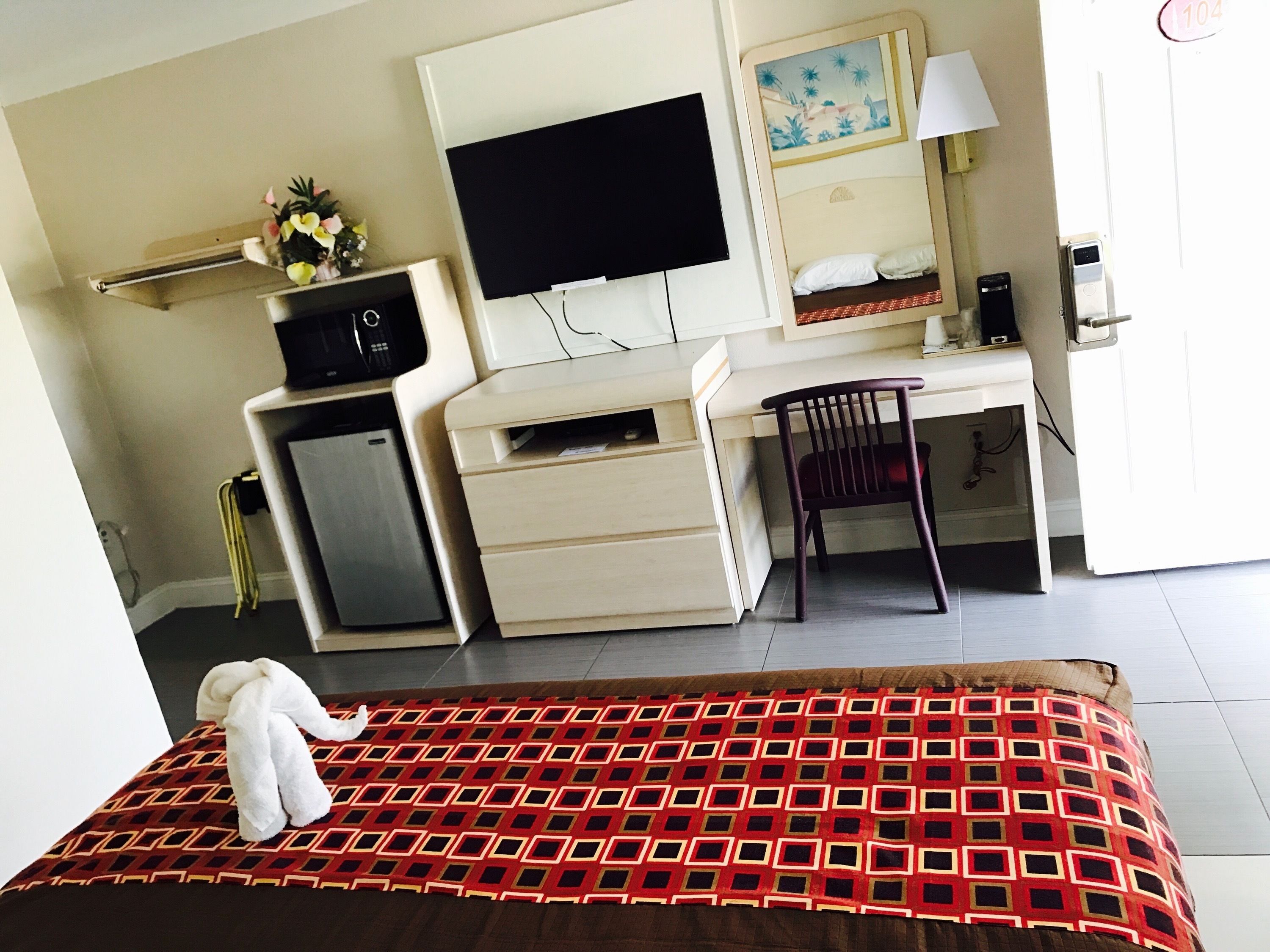Ein Hotelzimmer mit einem Bett, einem Schreibtisch, einem Sessel, einem Fernseher, einer kleinen Kühlbox und einer Lampe.