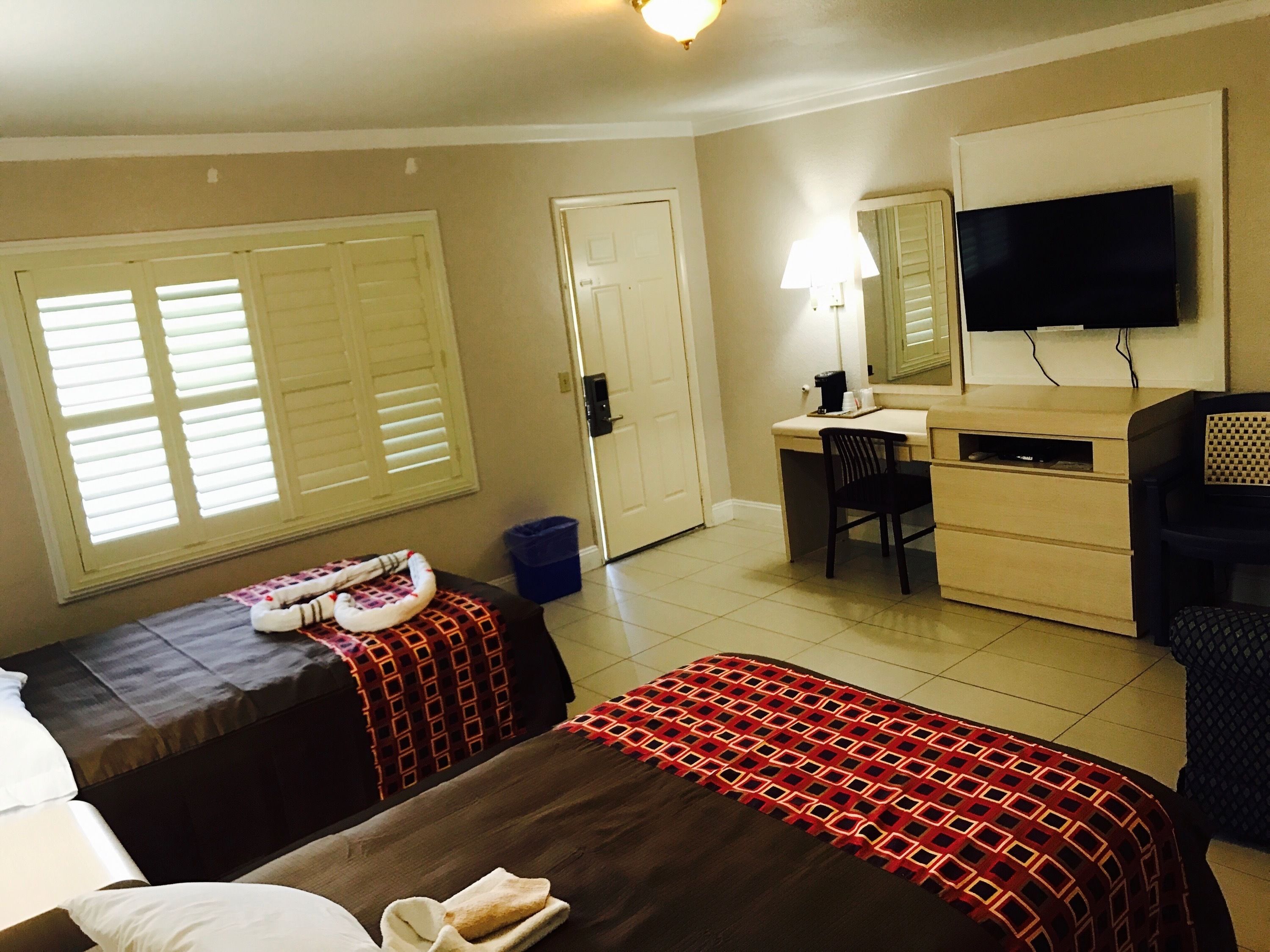 A hotel room with two beds, a desk, a chair, a television, and a window with blinds.