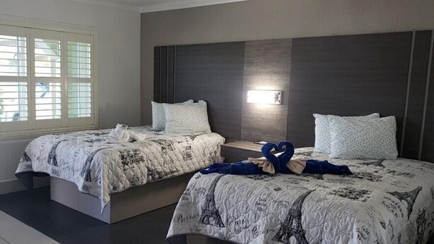 A hotel room with two beds, a large window, and a dark headboard. - Apollo Inn Motel (Cocoa)