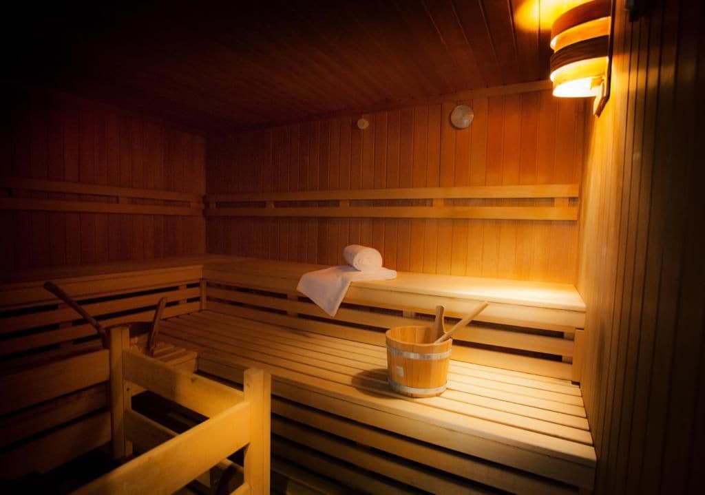 A sauna with wooden benches, a bench with a towel, and a bucket with a wooden stick.