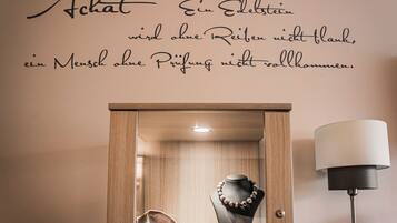 Eine Wand mit einem Zitat in Deutsch, eine Holzkassette mit Schmuck und eine Stehlampe.