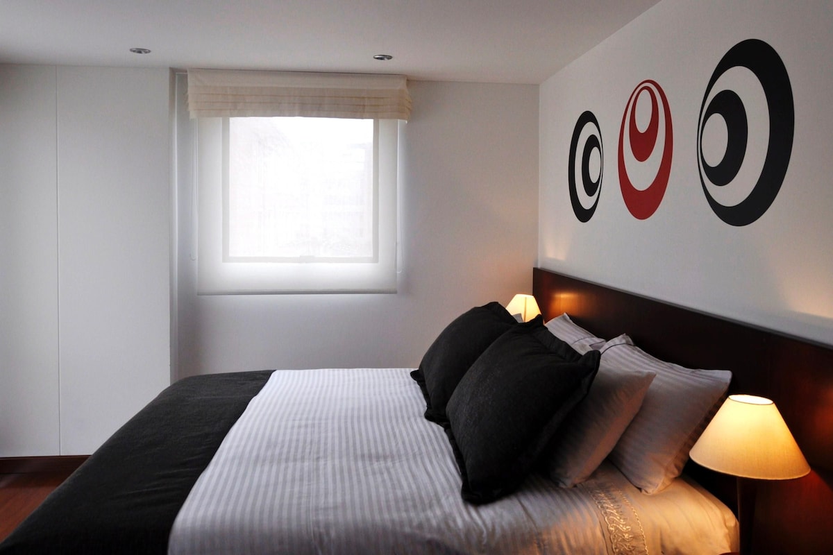Una habitación de hotel con una cama, un ventanal con cortinas y una pared decorada con diseños circulares.