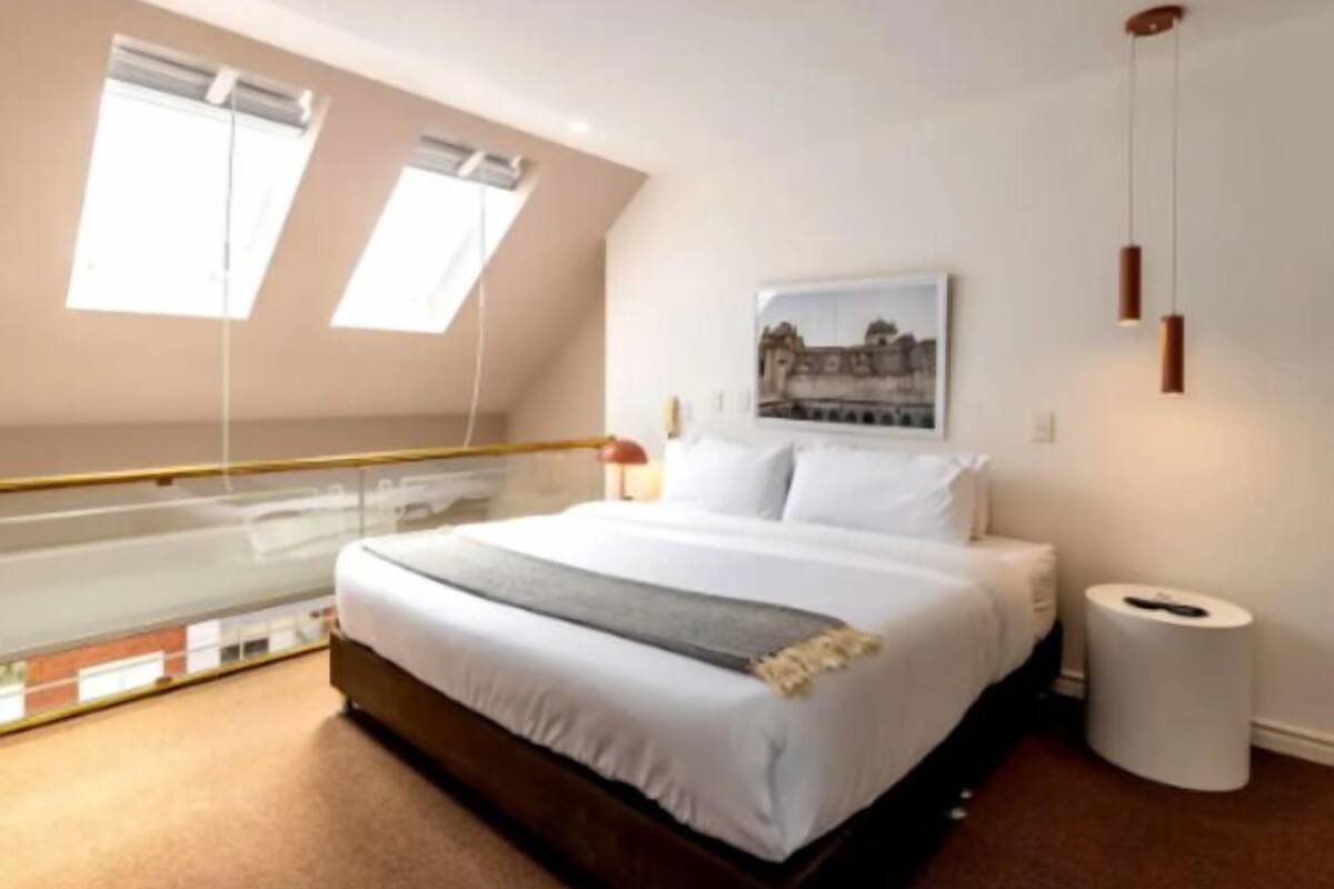 Una camera da letto con un letto, una finestra, un quadro appeso e un cestino.