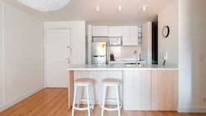 Une cuisine moderne avec des meubles blancs, un îlot central doté de tabourets, un four à micro-ondes et un réfrigérateur.