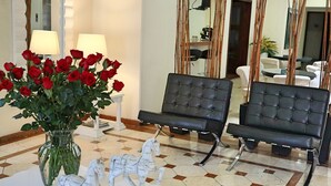 Un hall d’entrée agrémenté d’un vase de roses rouges, de deux fauteuils en cuir noir, d’une sculpture équestre blanche et d’un grand miroir.