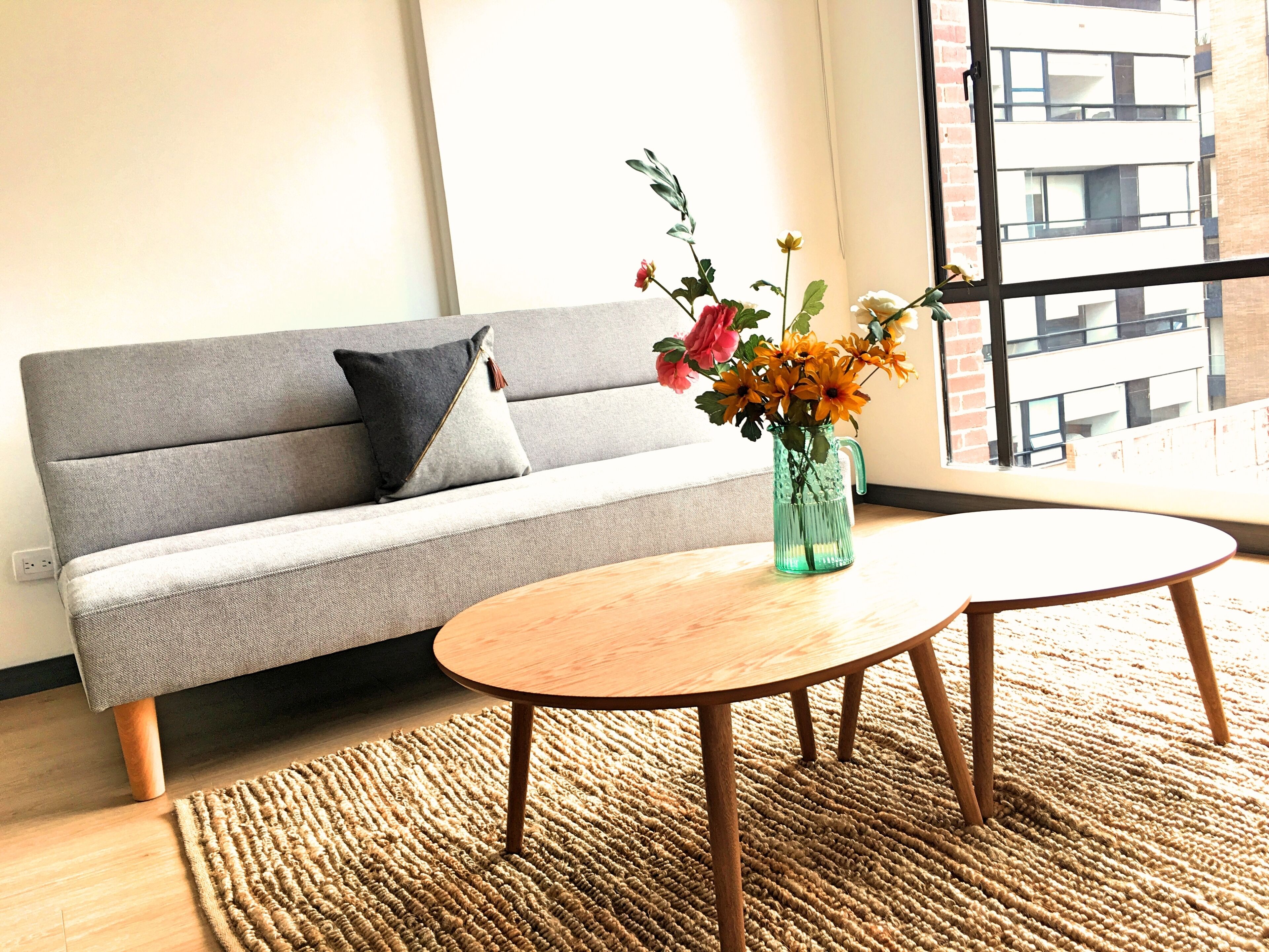 A modern living room with a grey sofa, a wooden coffee table, and a vase with flowers.
