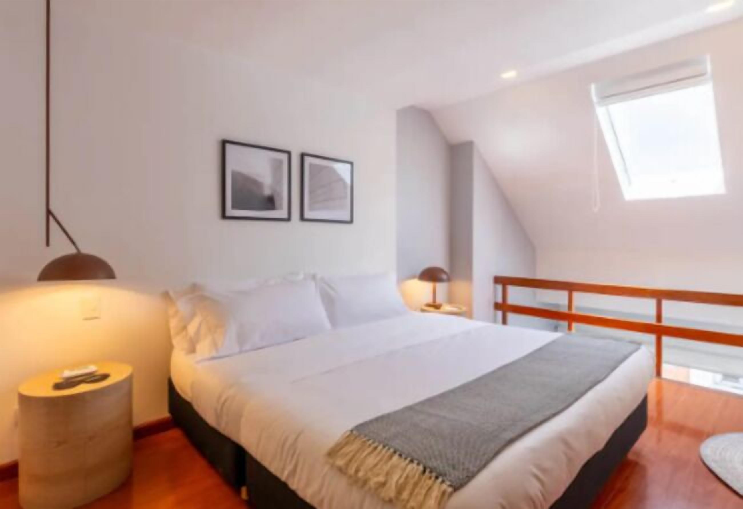 A bedroom with a bed, a bedside table, a lamp, and a window.
