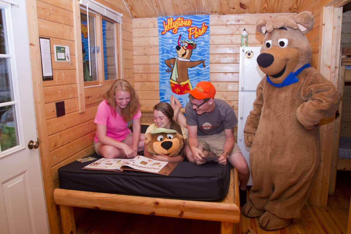 L’intérieur d’une cabane en bois, avec un lit, une affiche d’un ours et une personne déguisée en ours.