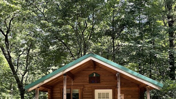 A wooden cabin with a porch, surrounded by trees. - Yogi Bear's Jellystone Park Camp-Resort Wisconsin Dells (Wisconsin Dells)