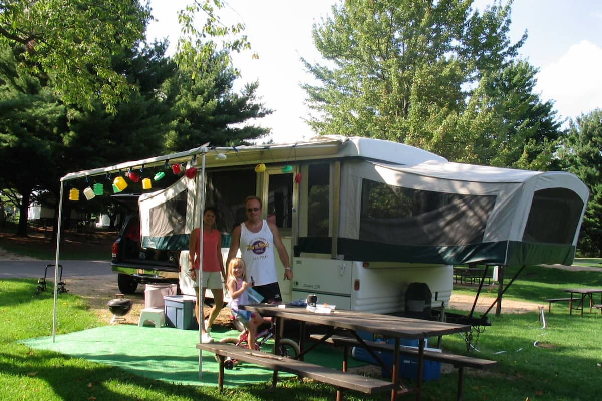 Un terrain de camping avec un camping-car blanc, des tables de pique-nique et une pelouse verte.