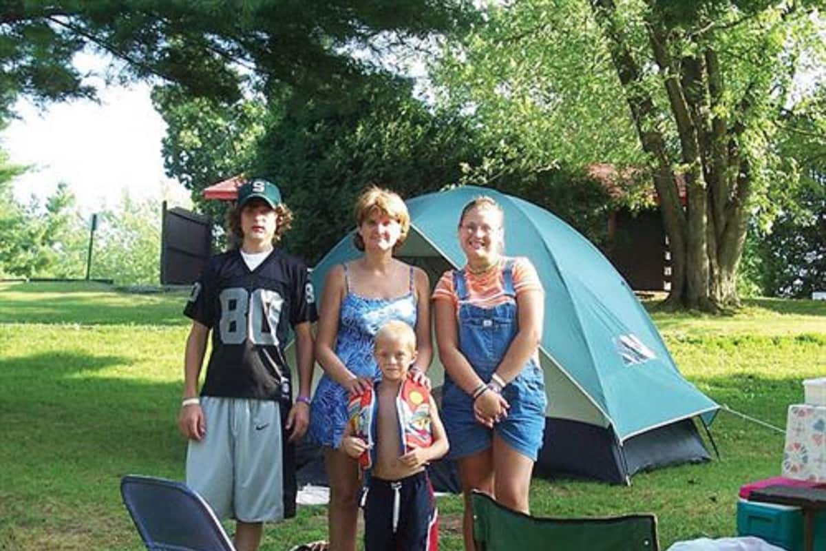 Une famille de quatre personnes se tient devant une tente, dans un espace herbeux.