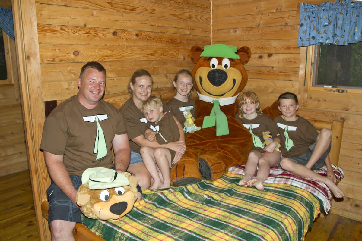 Une famille dans une cabane, avec une grande peluche en forme d’ours.