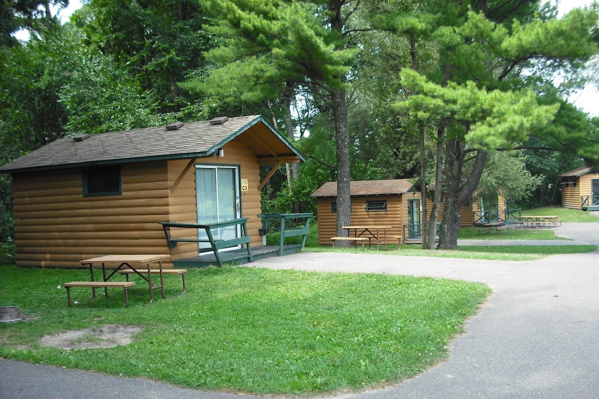 Une cabane en rondins avec une table de pique-nique et des bancs, située dans une zone boisée.