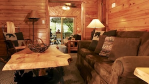 A cozy cabin interior with a wooden table, a leather sofa, and a dining area with chairs and a table. - Yogi Bear's Jellystone Park Camp-Resort Wisconsin Dells (Wisconsin Dells)