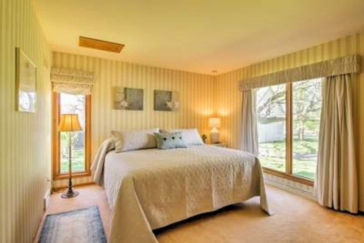 Une chambre avec un grand lit, deux lampes de chevet, une fenêtre avec des rideaux et une vue sur la verdure.