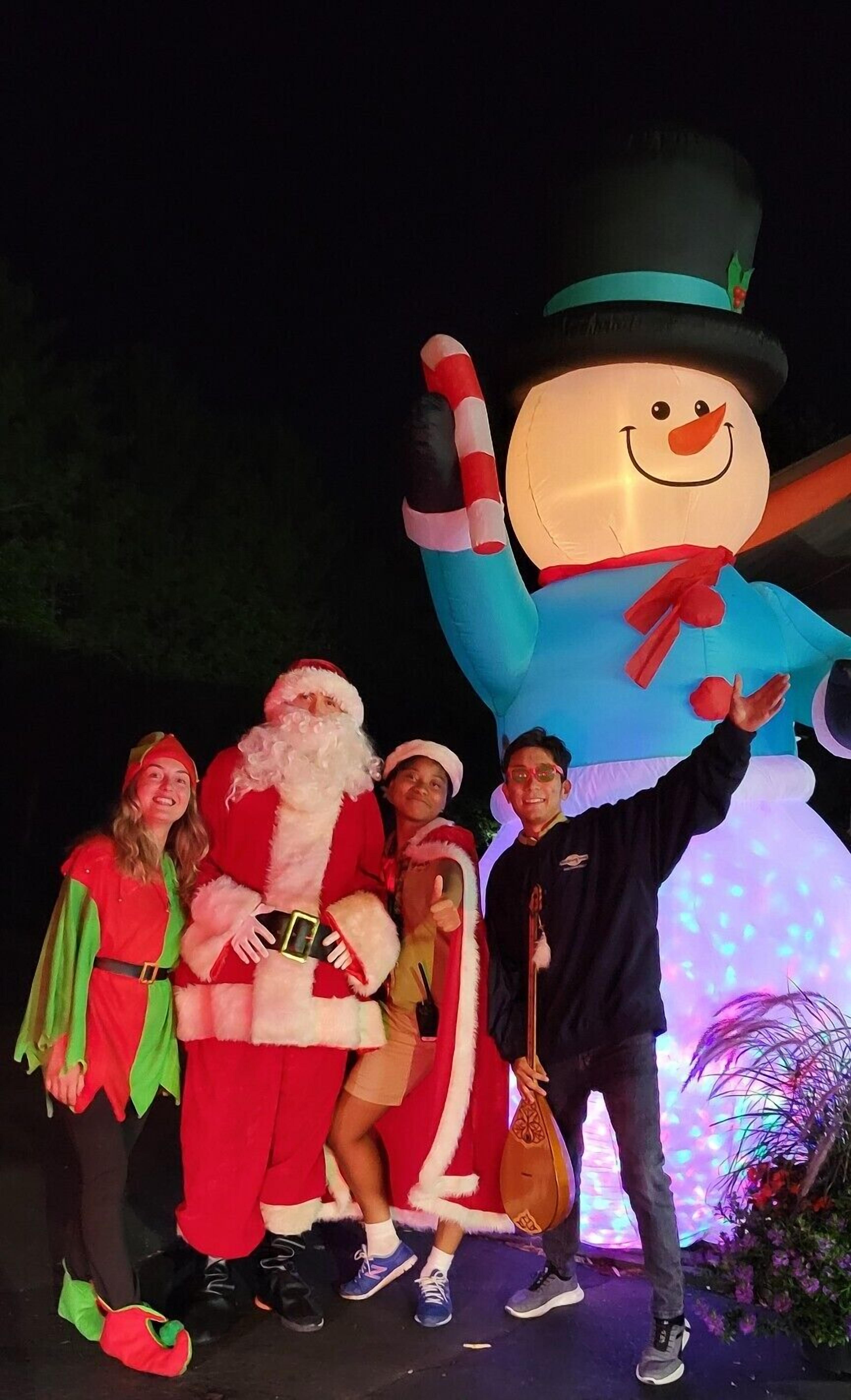 A group of people posing with a large inflatable snowman and Santa Claus.