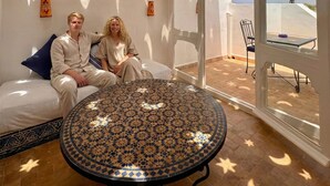 Una habitación con piso estampado, una mesa redonda y vistas a un espacio exterior con una mesa y sillas a través de un vano.