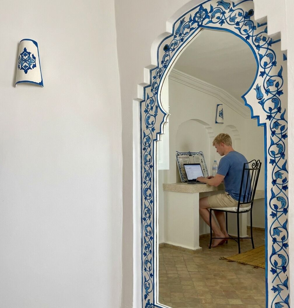 A room with a white and blue ornate mirror frame, a laptop on a table, and a chair.
