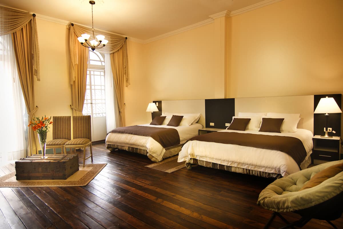 A hotel room with two beds, a sitting area with a chair, a small table, and a vase of flowers.