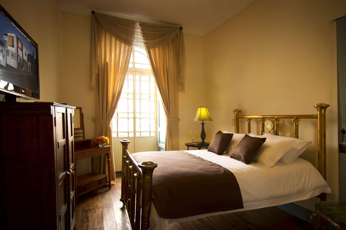 A hotel room with a bed, a television, a lamp, and a window with curtains.