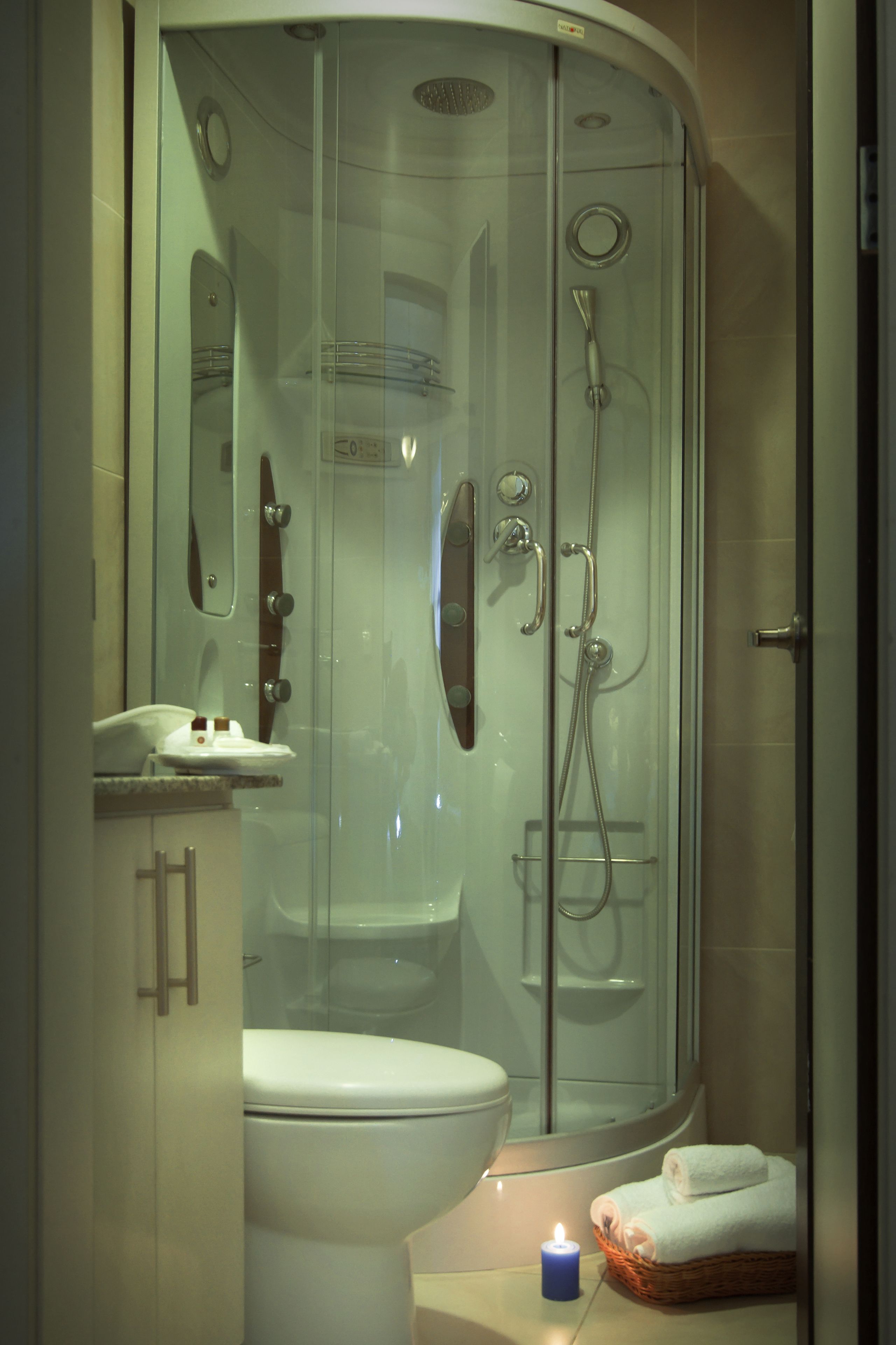 A modern bathroom with a glass-enclosed shower, a toilet, and a small wicker basket with towels.