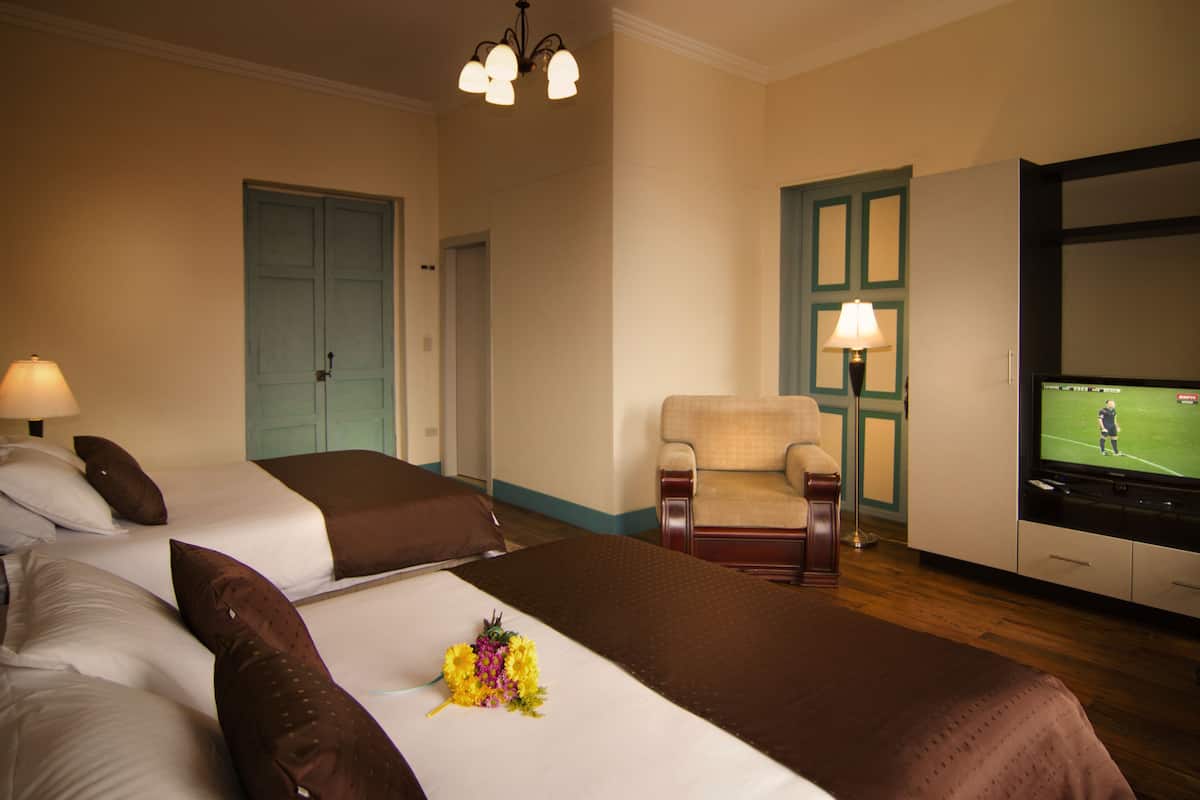 A hotel room with two beds, a chair, a television, and a door.