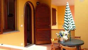 A room with a wooden door, a window, and a table with a striped umbrella. - La Fonte degli Angeli (Suvereto)