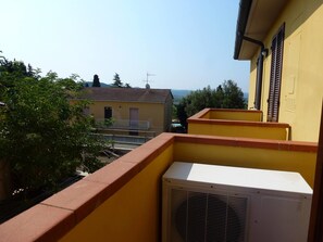 A yellow building with a balcony, an air conditioning unit, and a view of a distant landscape.