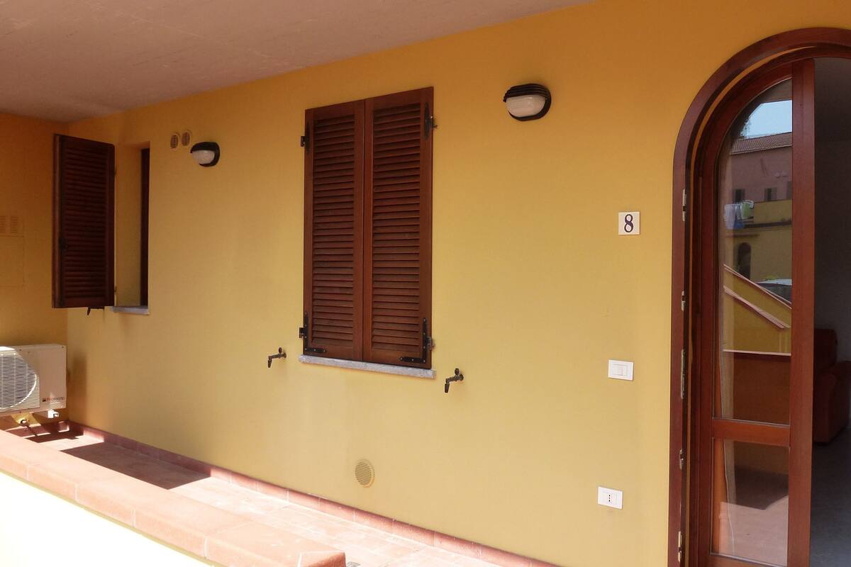Un bâtiment jaune avec des volets en bois, un escalier et un numéro de chambre, le 8, clairement visible.