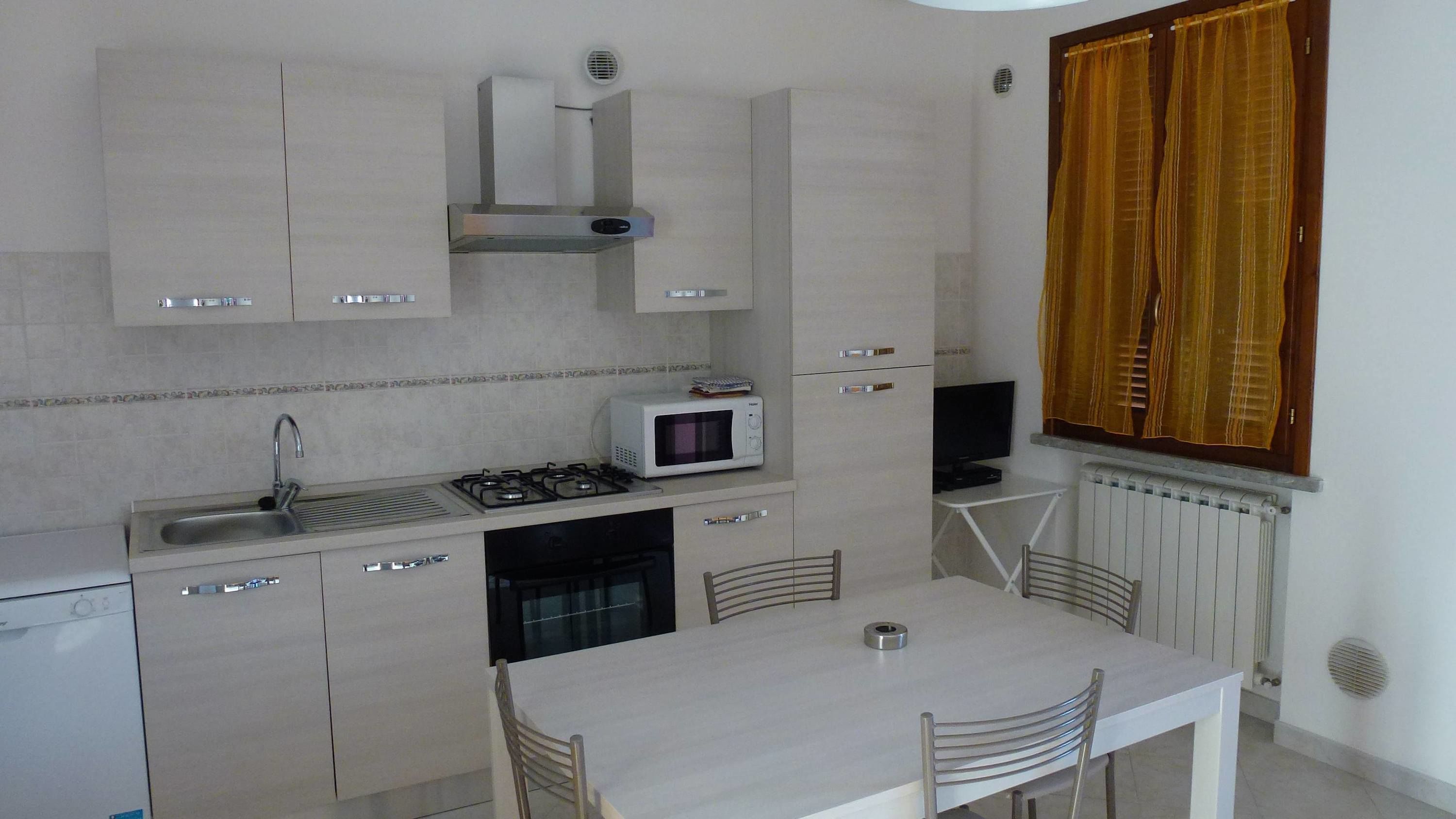 A compact kitchen with a gas stove, microwave, and a small dining table with chairs.