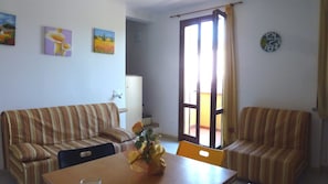 Un salon avec deux canapés à rayures, une table à manger ornée d’un vase de fleurs et une horloge au mur.