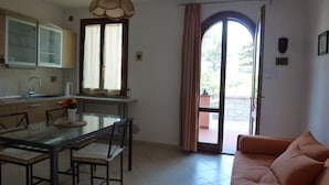 A compact kitchen with a dining area, a sofa, and a sliding glass door leading to an outdoor area. - La Fonte degli Angeli (Suvereto)