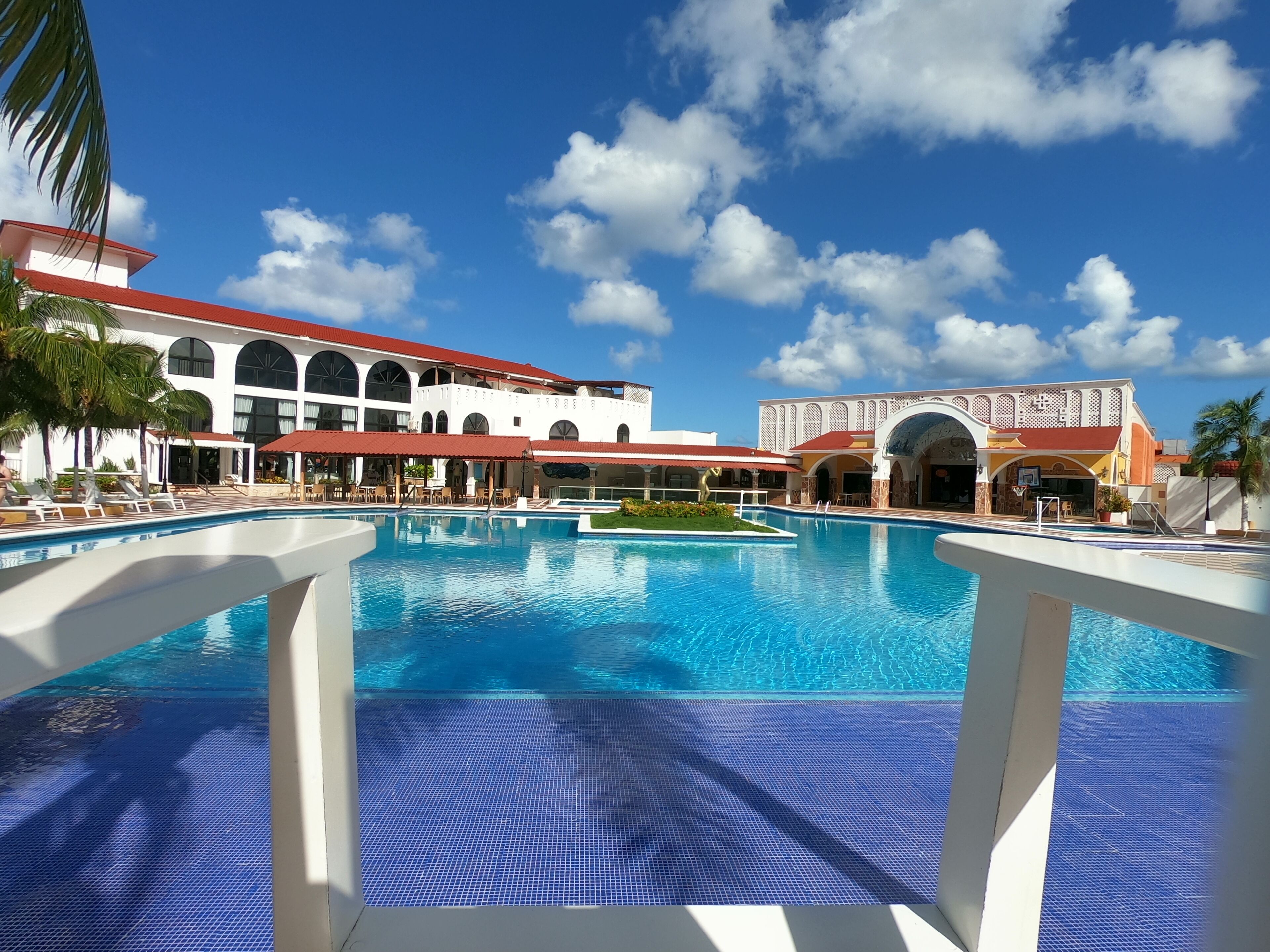 A large outdoor swimming pool with a clear blue sky and white buildings in the background.