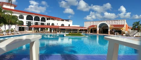 A large outdoor swimming pool with a clear blue sky and white buildings in the background.