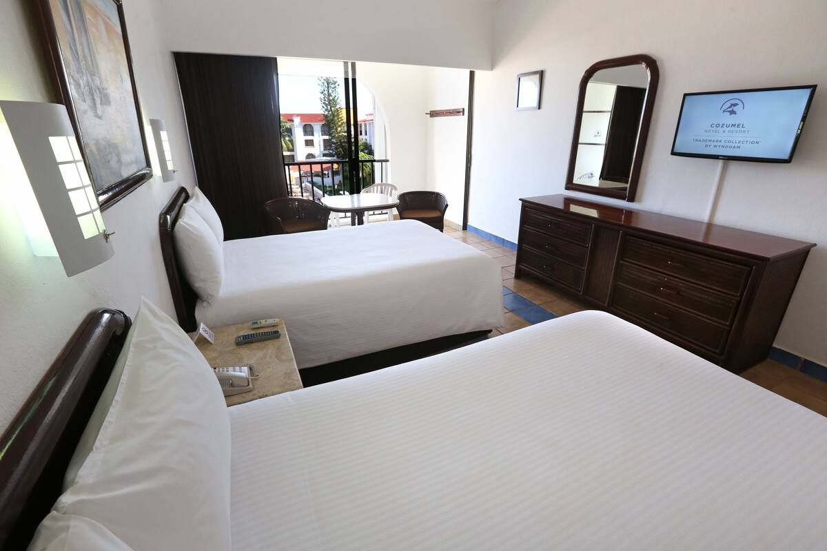 Une chambre d’hôtel avec deux lits, une télévision, une commode et une fenêtre donnant sur les bâtiments environnants.