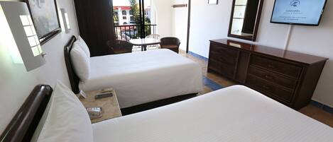 Habitación de hotel con dos camas, televisor, cómoda y ventana con vistas a edificios.