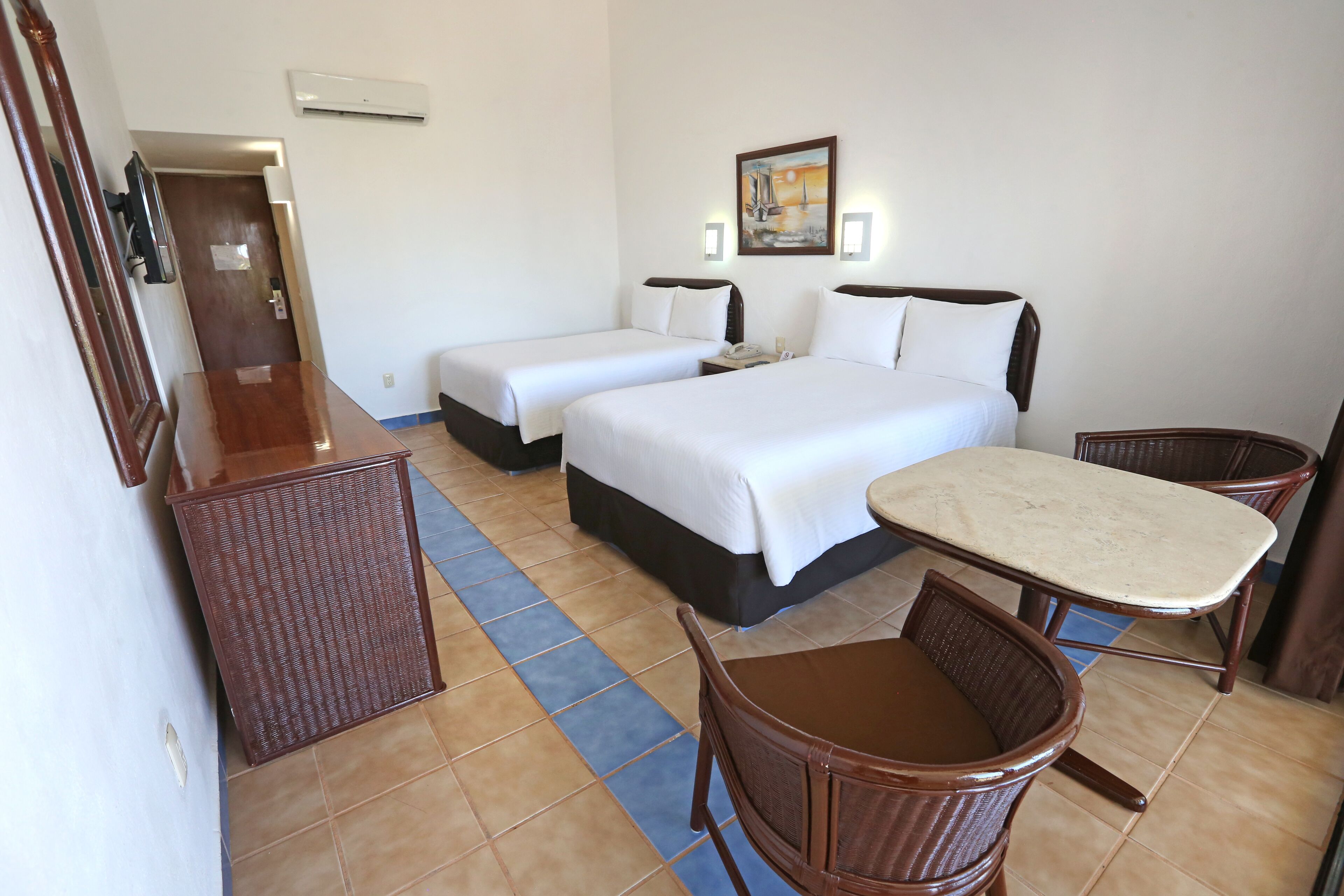 A hotel room with two beds, a small table, two chairs, a desk, and a mirror.