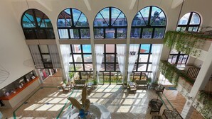 Un hall espacioso con amplias ventanas arqueadas, una recepción y una fuente central.