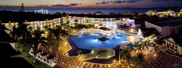 Un resort con una amplia piscina, varias edificaciones y palmeras.