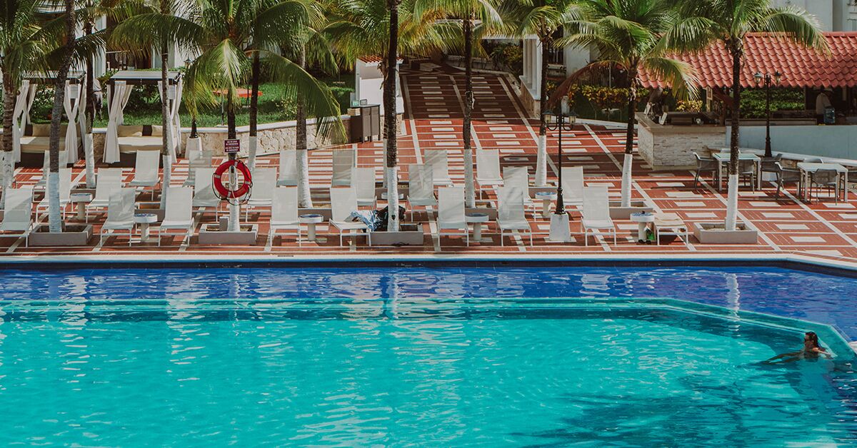 A pool area with white lounge chairs and palm trees.