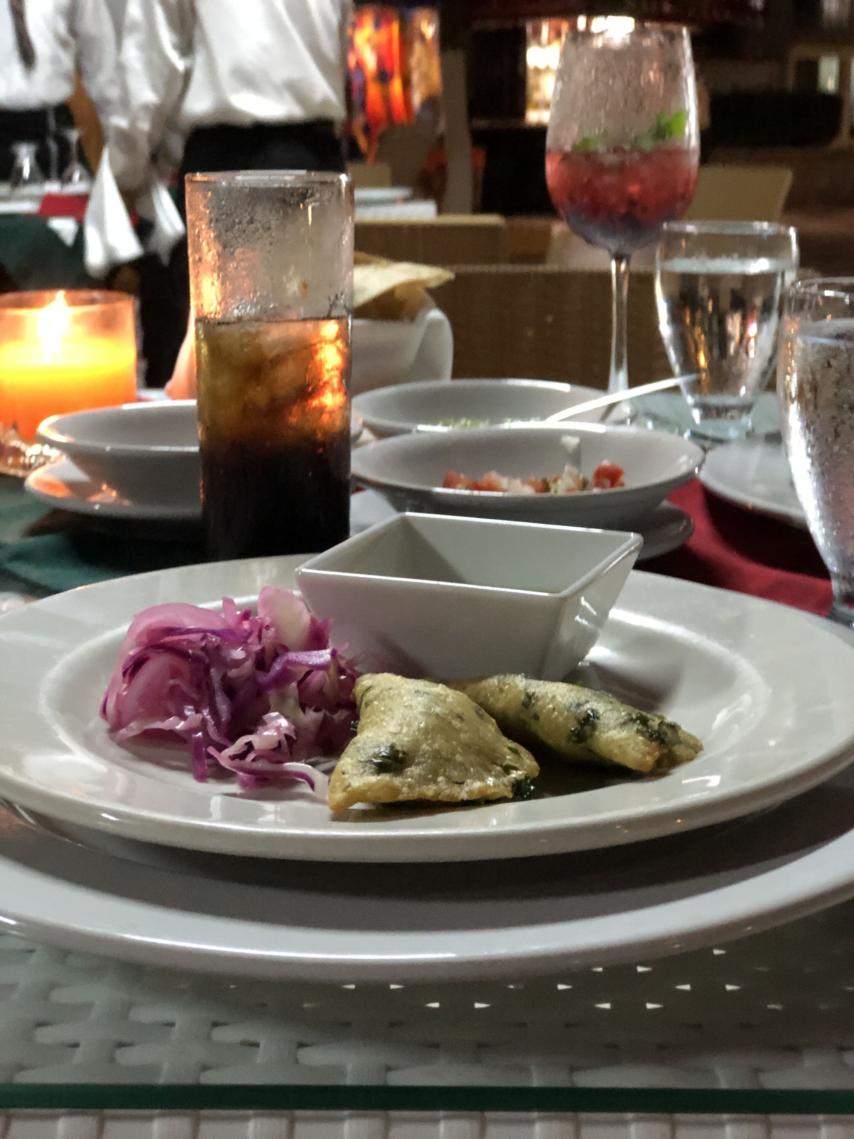 A dining table with a plate of food, a glass of iced beverage, and a candle.
