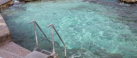 A clear pool with steps leading into it, surrounded by rocky formations.