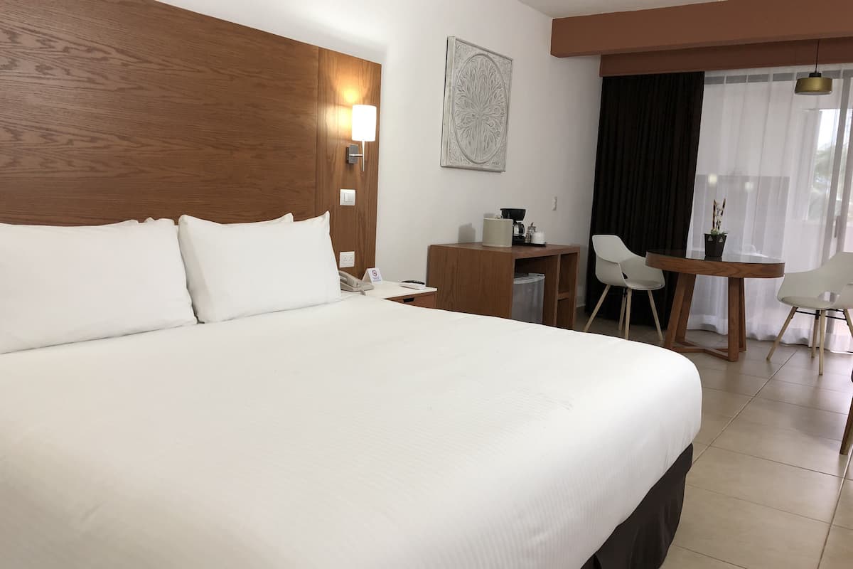 Une chambre d’hôtel avec un grand lit, un bureau avec une chaise, une petite table avec une chaise et une fenêtre avec des rideaux.