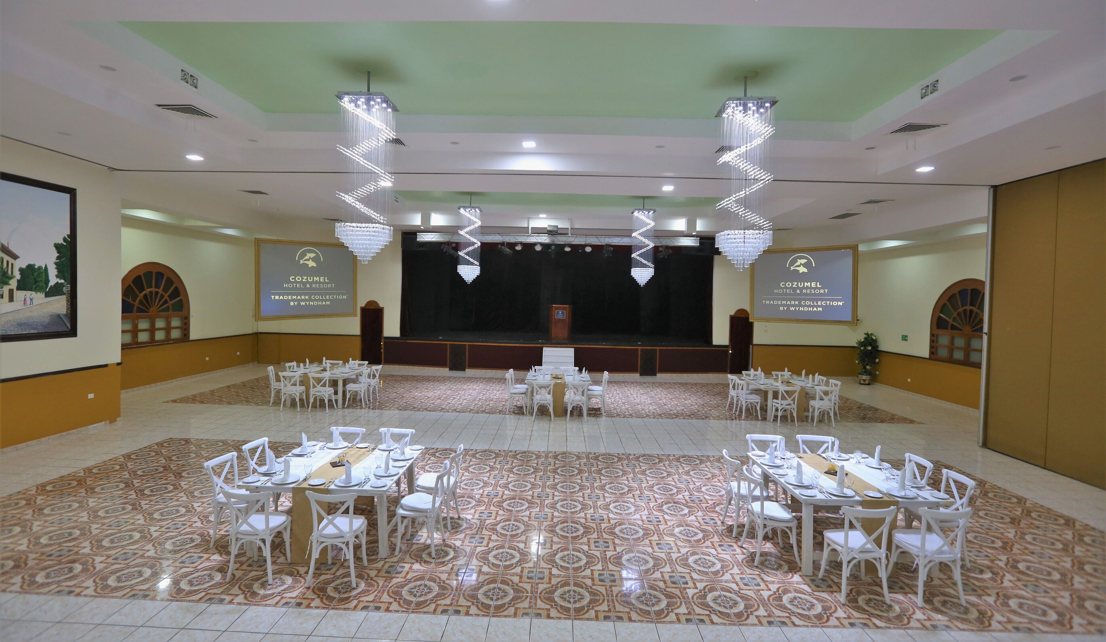 Un salón de conferencias con un escenario, sillas blancas y mesas dispuestas para una reunión.