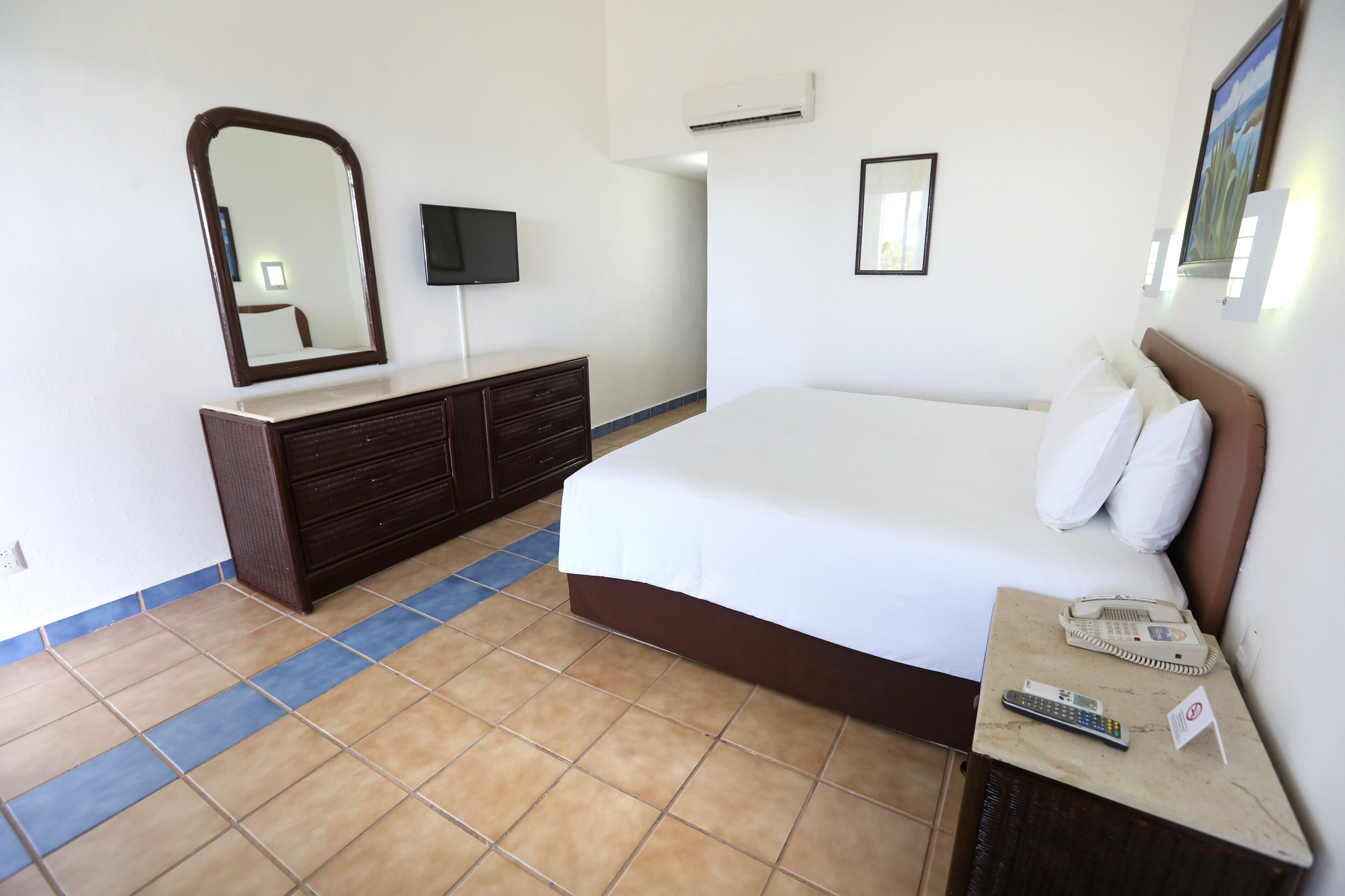 A hotel room with a bed, dresser, mirror, TV, and a phone on the bedside table.