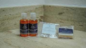 A bathroom counter with two bottles of organic honey shampoo, a package of makeup remover wipes, and a bar of organic aloe soap.