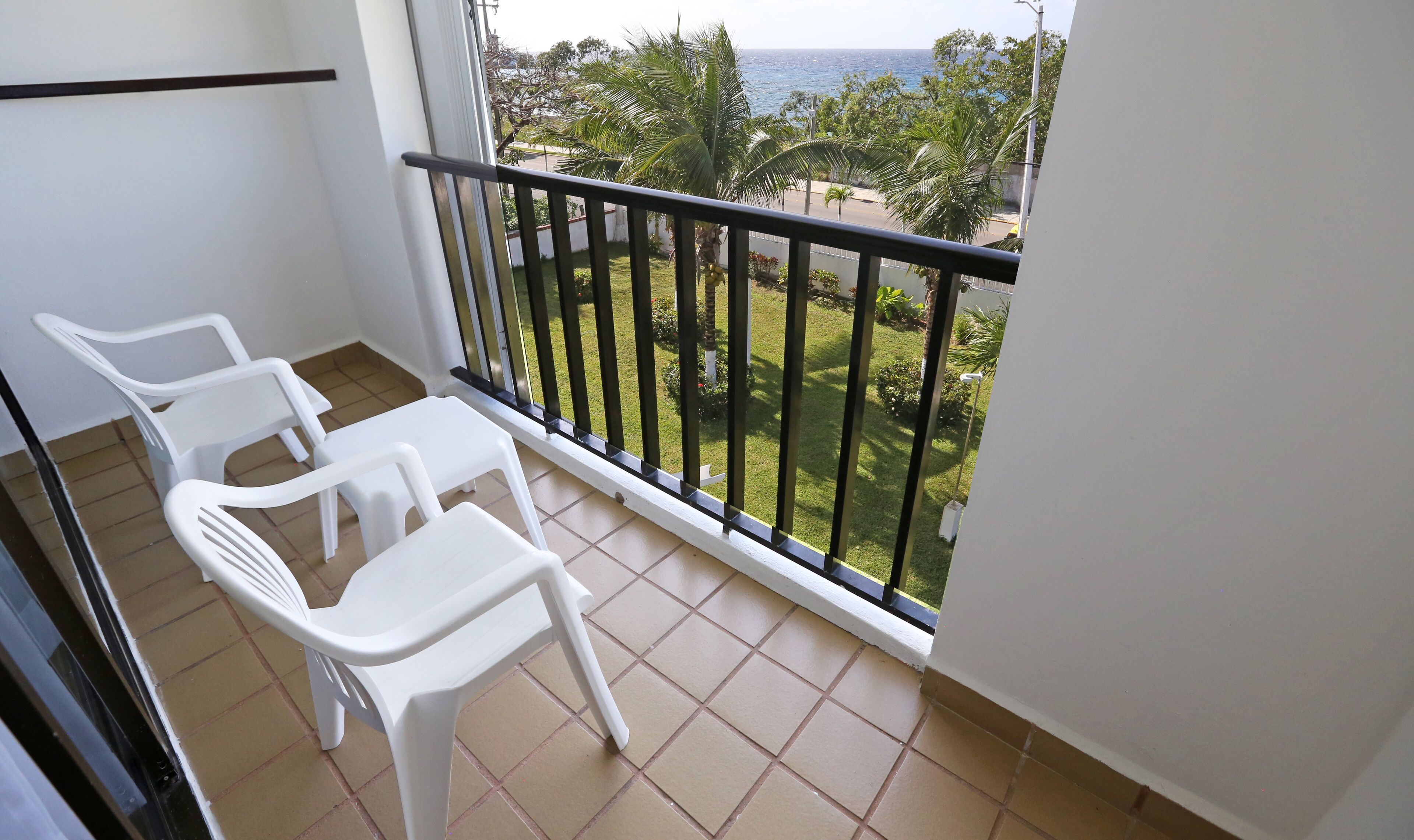 Un balcon avec des chaises en plastique blanches et une vue sur la mer et la verdure.