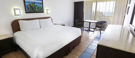 Habitación de hotel con una cama grande, una mesita, una silla y un balcón con vistas.