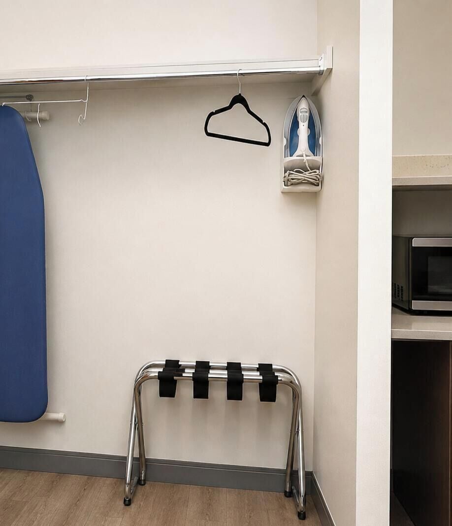A room with a metal rack with black straps, a blue garment hanging, and a white iron on a shelf.
